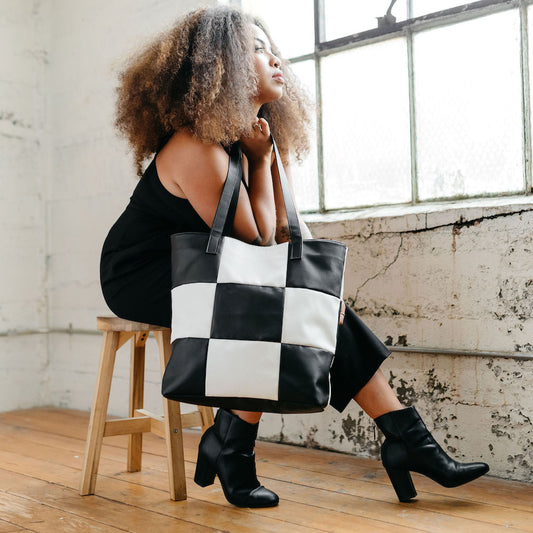 Model holding vegan leather black and white checker tote bag gazing out a window.