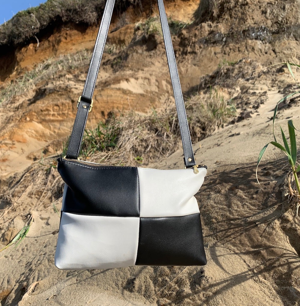 Handmade black and white checker purse made from cactus leather. Held in front of cliffy beach landscape