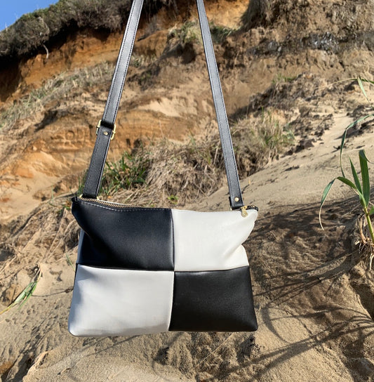 Handmade black and white checker purse made from cactus leather. Held in front of cliffy beach landscape